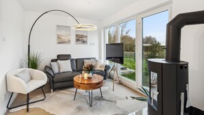 A modern living room with a sofa, armchair, and coffee table, a fireplace, and large windows offering a view of the outdoors. - Gorgeous home in Tossens with sauna (Tossens)