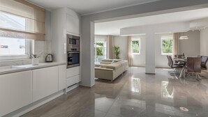 A modern kitchen with built-in appliances, a dining area with a glass table, and a living space with a sofa and a plant. - Beautiful home in Barbariga (Barbariga)