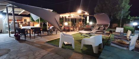 Un patio al aire libre con suelo de piedra, sillas de plástico blanco y una mesa de comedor.