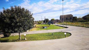 A paved pathway curving through a grassy area with a large tree and a building in the background. - Holiday home in a quiet location (Modica)