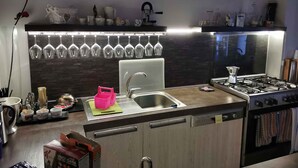 A modern kitchen with a stainless steel sink, a gas stove, and a wine rack with multiple glasses. - Holiday home in a quiet location (Modica)