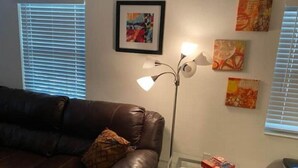 A living room with a brown leather couch, a glass coffee table, a floor lamp, and framed artwork on the wall. - Beach within Reach Apt 1 (Clearwater)