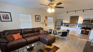 A modern living room with a brown leather sofa, a glass coffee table, and a dining area with a small table and chairs. - Beach within Reach Apt 1 (Clearwater)