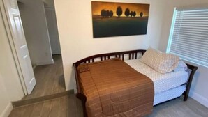 A bedroom with a bed, a painting on the wall, and a window with blinds. - Beach within Reach Apt 1 (Clearwater)