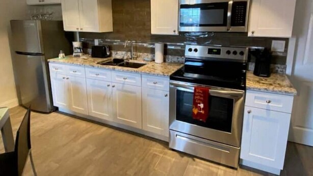 A modern kitchen with white cabinets, stainless steel appliances, a granite countertop, and a built-in oven. - Beach within Reach Apt 1 (Clearwater)