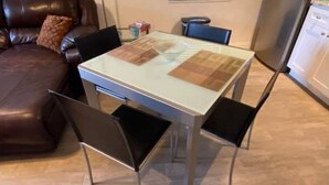 A dining area with a glass-top table, four chairs, a brown leather couch, and a refrigerator in the background. - Beach within Reach Apt 1 (Clearwater)