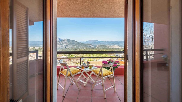 A balcony with a table and chairs, a view of mountains, and a red railing. - Holiday home with a/c (Dorgali)