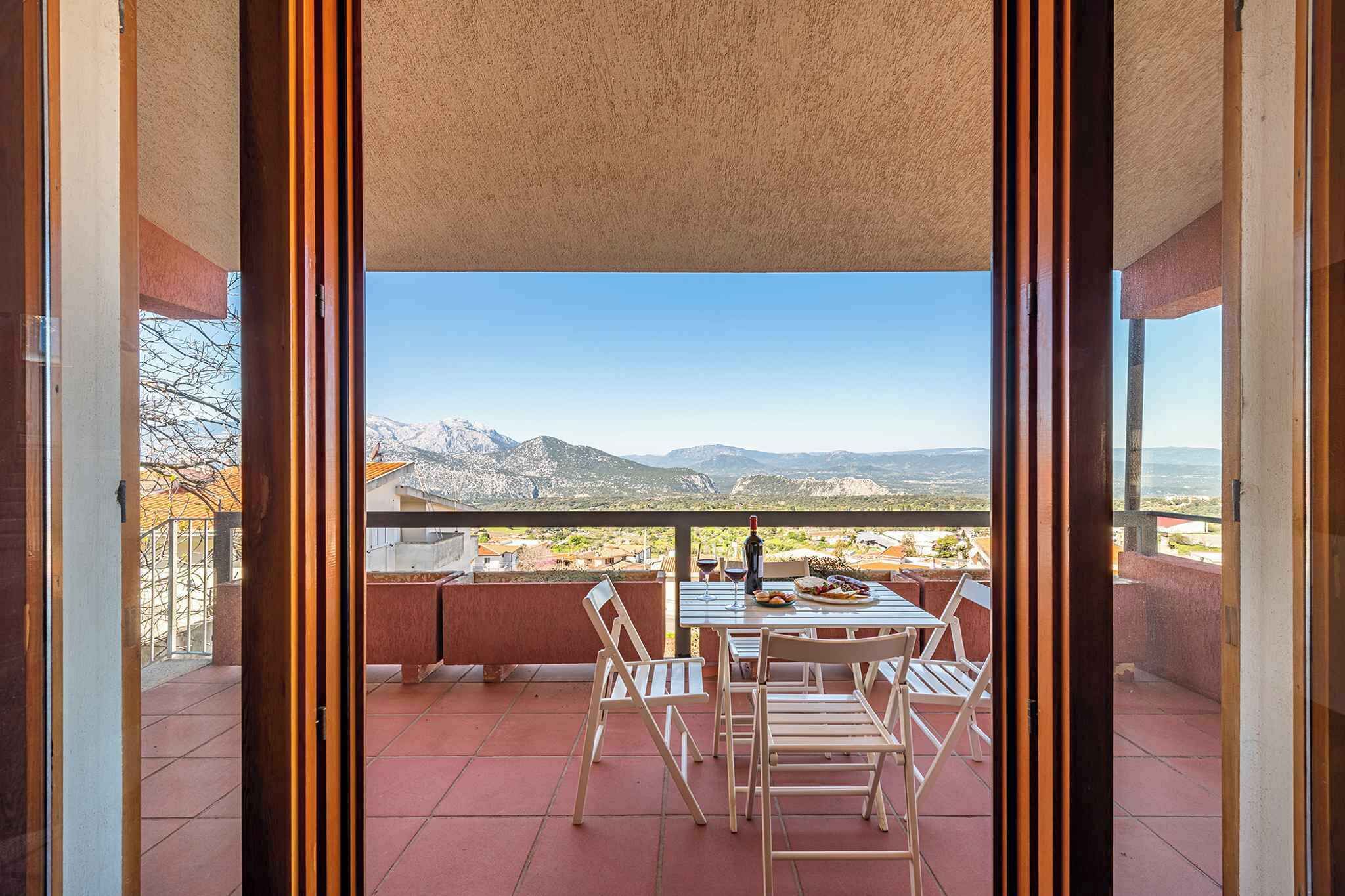 A balcony with a table and chairs, overlooking a mountainous landscape.