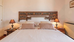 A double bed with a patterned headboard, two bedside tables with lamps, and a small table with a teapot and cups. - Holiday home with a/c (Dorgali)