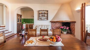 A dining area with a wooden table set for a meal, a fireplace, and a green-tiled backsplash in the background. - Holiday home with a/c (Dorgali)