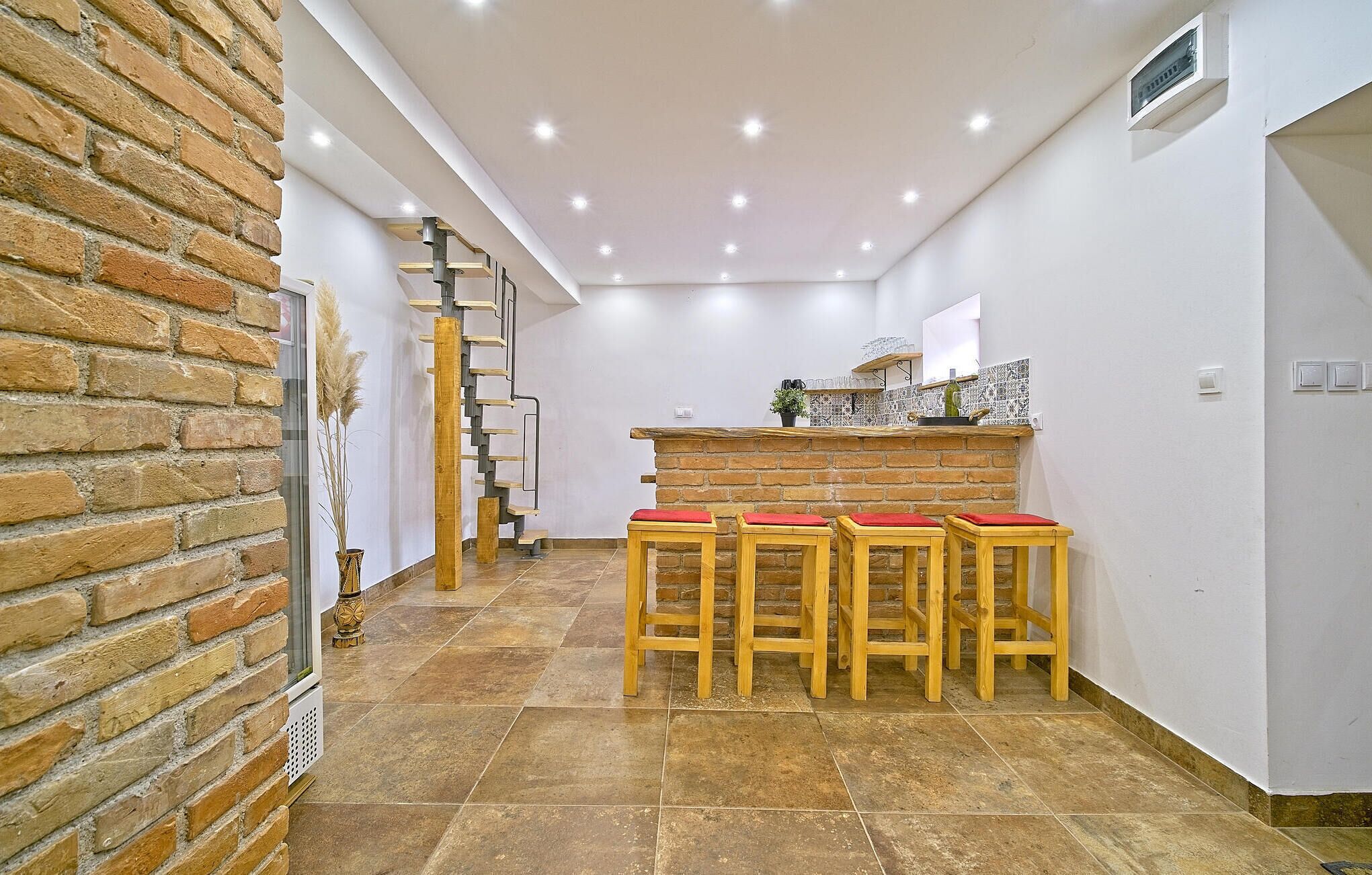 Une cuisine moderne avec un mur en briques, un escalier en bois et un coin bar avec des tabourets.