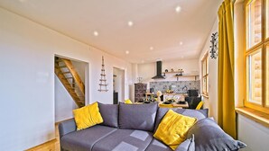A modern living room with a grey sofa and yellow cushions, a staircase, and a kitchen in the background. - Amazing home in Dragovanscak (Dragovanscak)
