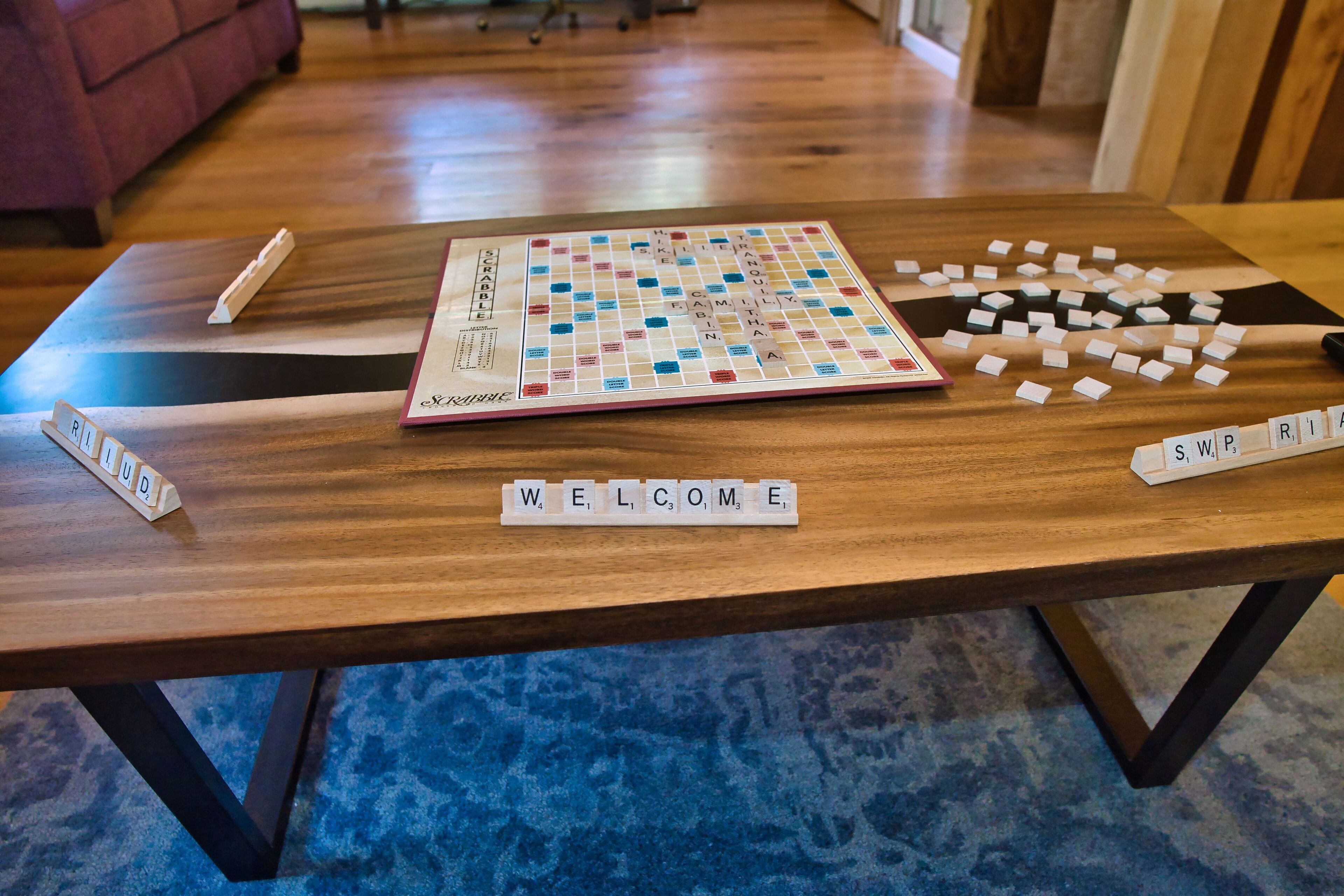 A Scrabble game on a wooden table with tiles scattered around and a welcome sign.