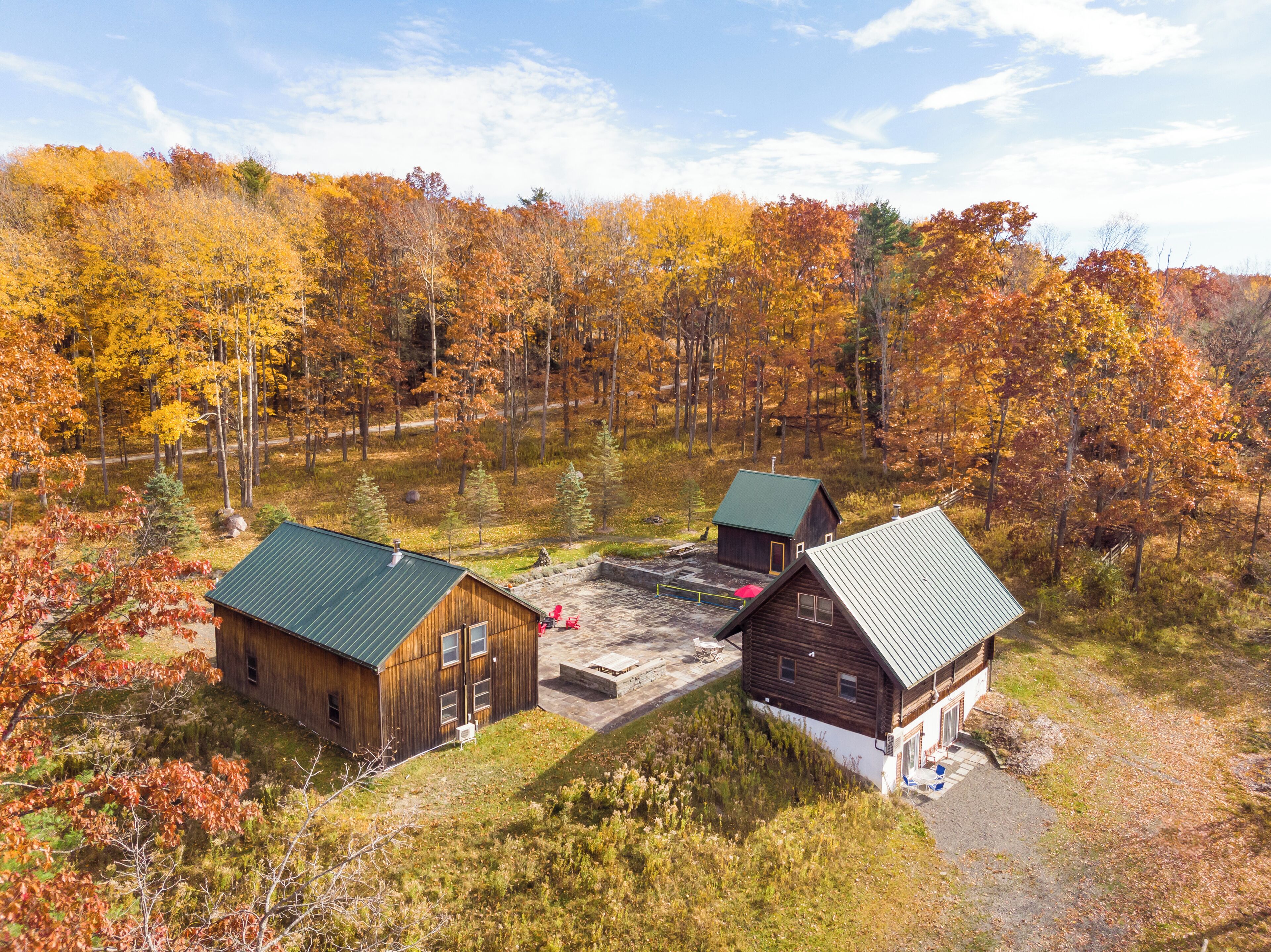 A cabin with a green roof and a small porch, surrounded by a forest with autumn foliage.
