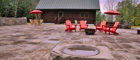 A wooden cabin with a stone patio, outdoor seating, and a stone well.