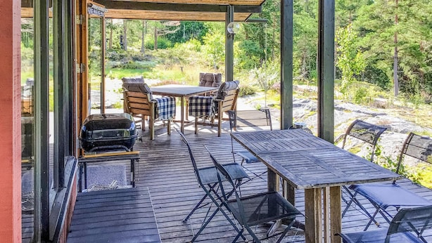 Un patio exterior con mesas y sillas de madera, una parrilla y vistas del bosque circundante.