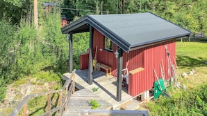 Una cabaña roja con un porche, una terraza de madera y una carretilla verde.