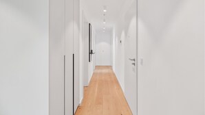 A narrow, well-lit hallway with white walls and wooden flooring, leading to a door at the end. - 2 bedroom amazing apartment in Tossens (Tossens)