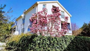 Un edificio de dos pisos con balcones, rodeado de follaje y árboles en flor.