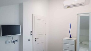 Una habitación con una puerta blanca, televisor montado, armario blanco y unidad de aire acondicionado en la pared.