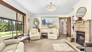 A spacious living room with a fireplace, two armchairs, a sofa, and a large painting. - Mountain Culture Farm Stays  (Kanimbla)