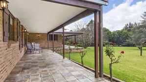 A covered patio area with a brick wall, a pergola, and a lawn. - Mountain Culture Farm Stays  (Kanimbla)