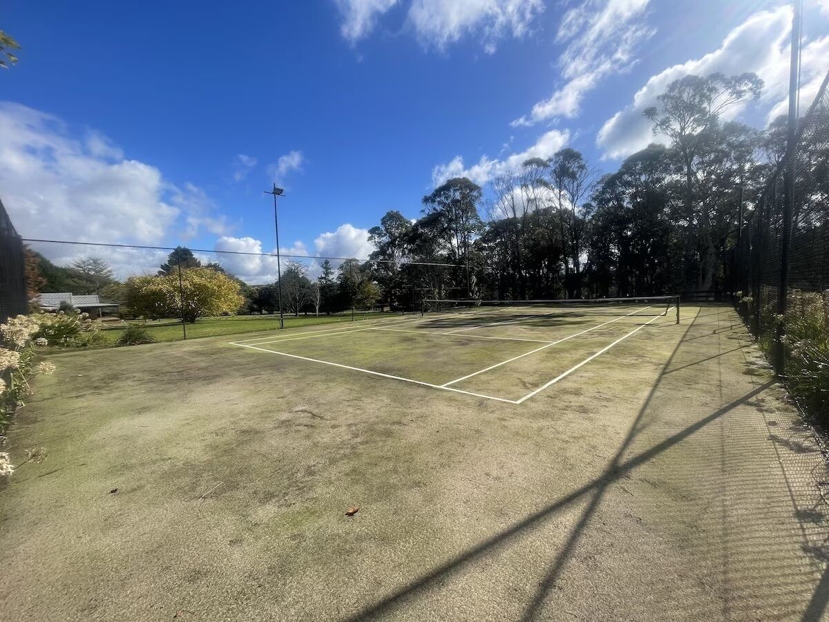 An outdoor tennis court with a net, surrounded by trees and a fence.