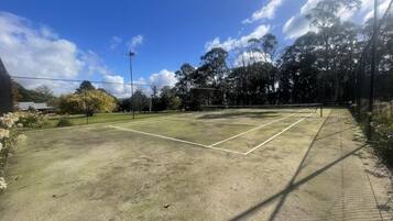 An outdoor tennis court with a net, surrounded by trees and a fence.