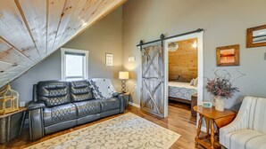 A cozy loft bedroom with a sloped ceiling, a gray leather sofa, a patterned rug, and a wooden bed frame. - Lovely Lakefront Apartment w/ Boat Ramp Access (Clifton)