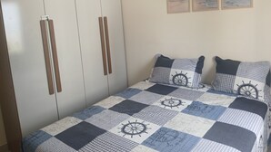 Ein Schlafzimmer mit einem Bett, das mit einer Schiffsdeko-Quiltdecke ausgestattet ist, einem zweitürigen Kleiderschrank und drei gerahmten Bildern an der Wand.
