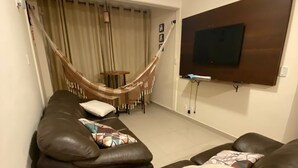Ein Wohnzimmer mit braunem Ledersofa, einer Hängematte und einem an der Wand befestigten Flachbildfernseher.