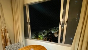 Ein kleiner Essbereich mit einem runden Holztisch und zwei Stühlen, ein großes Fenster mit Blick auf Palmen und eine hängende Leuchte.