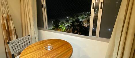 A small dining area with a round wooden table and two chairs, a large window with a view of palm trees, and a hanging light fixture.