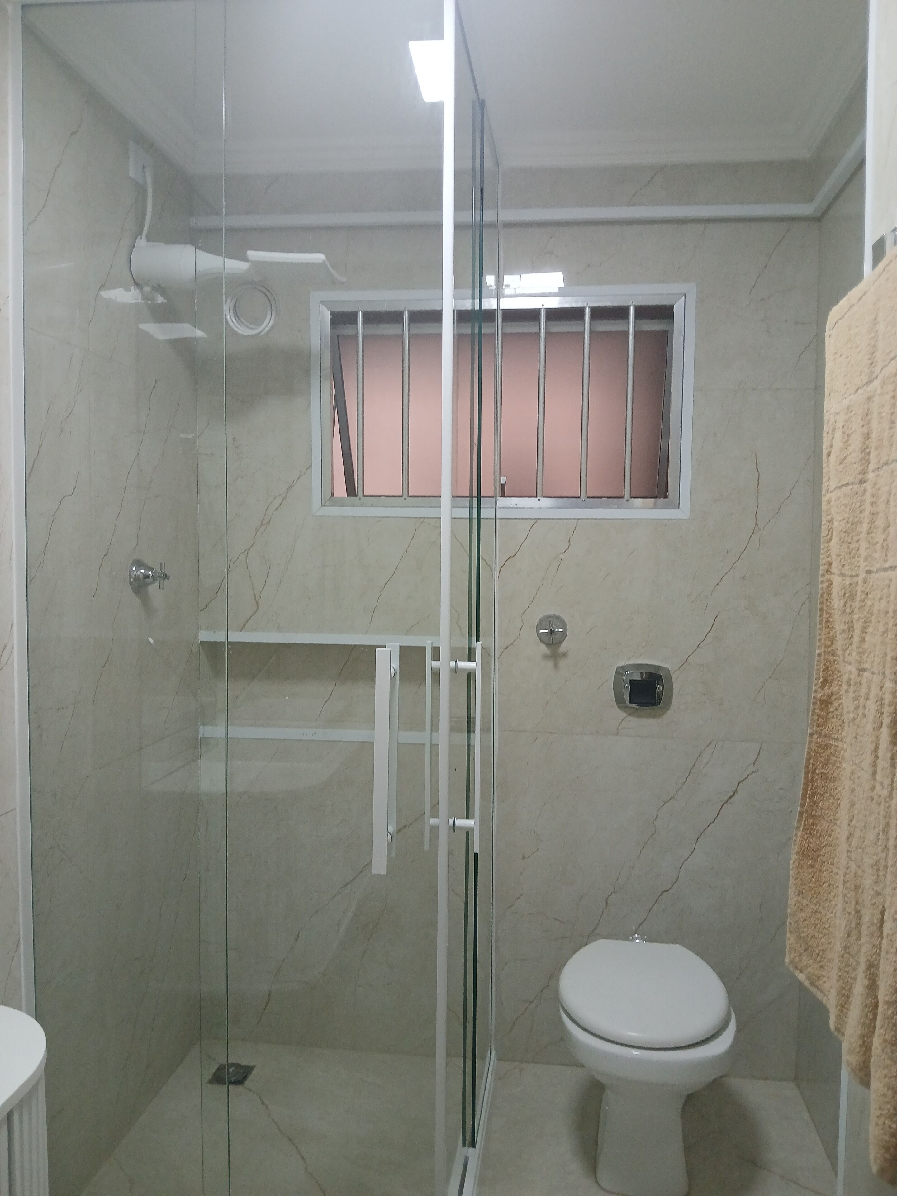 Ein Badezimmer mit Duschkabine, Toilette und einem Fenster mit rosa Innenraum.