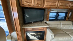 A cozy RV interior with a flat-screen TV mounted on a wooden cabinet, a comfortable beige couch, and a small oven below the TV. - Enjoy your stay in luxury at Grange for PSU Tailgate, or our Private Lot w/Pool (Bellefonte)