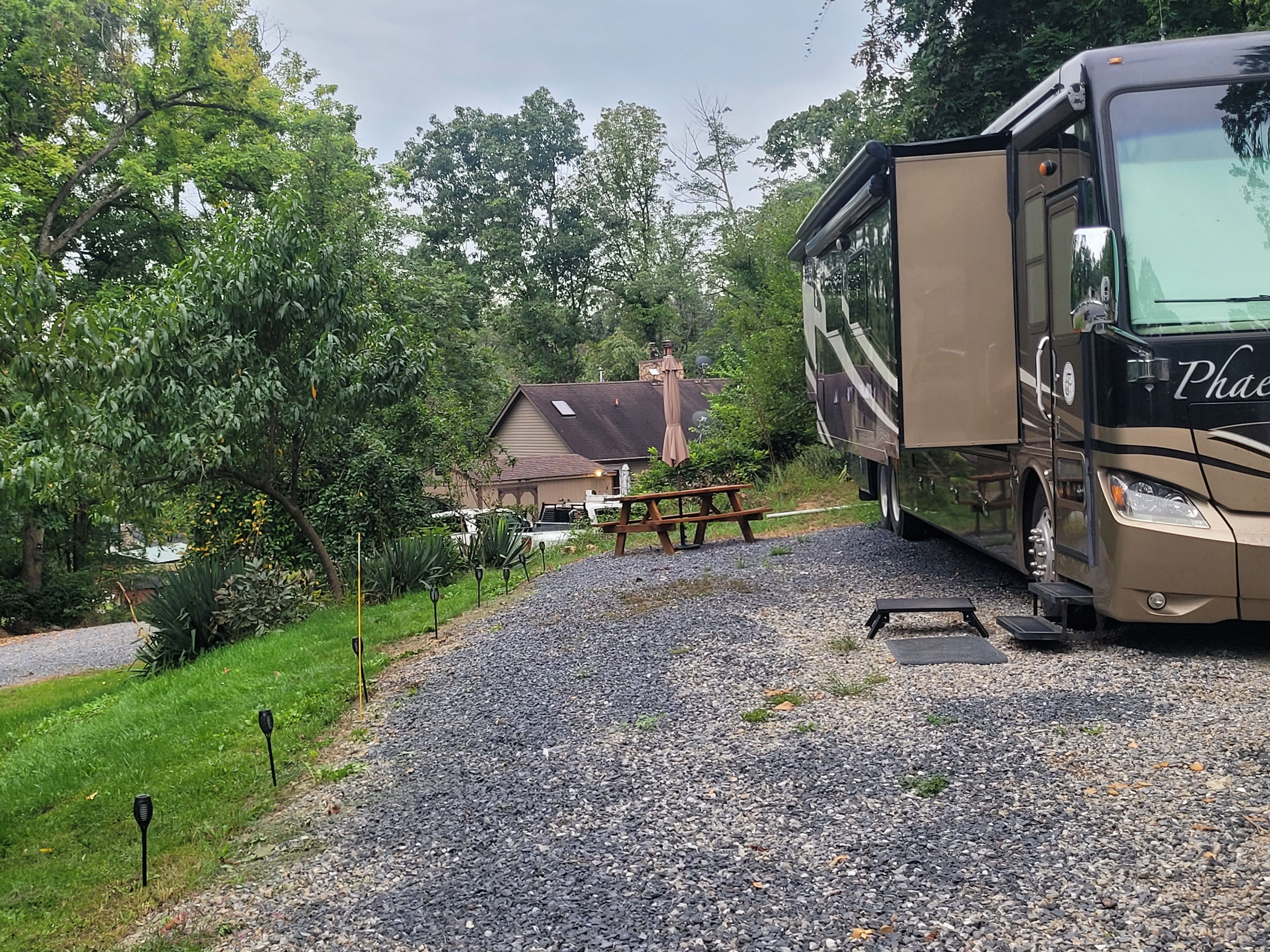 Un camino de grava que lleva a una casa con una mesa de picnic y una caravana grande estacionada cerca.