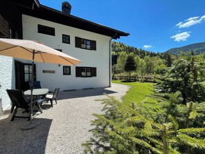 Guests can enjoy a patio area with a table and chairs, surrounded by lush greenery and a mountain view.