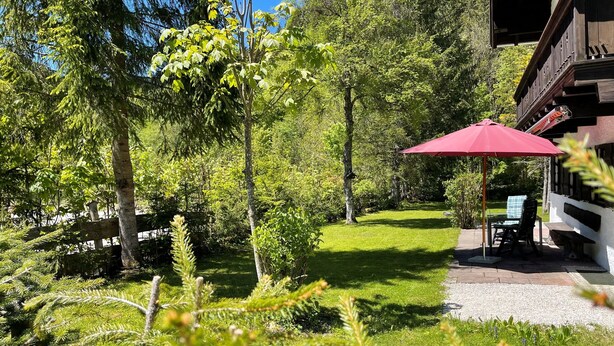 A garden with a red umbrella, a wooden fence, and a building with a balcony. - Forsthaus Fewo 10 OG (Reit im Winkl)