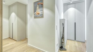 Un couloir avec un aspirateur, un tableau encadré accroché au mur et une porte dotée d’une poignée.