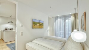 A modern bedroom with a bed, a small kitchenette, and a large window with curtains. - 1 bedroom amazing apartment in Tossens (Tossens)