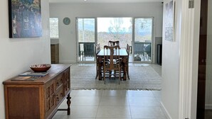 A spacious dining area with a wooden table and chairs, a wooden cabinet with drawers, and a large window offering a view of the outdoors.