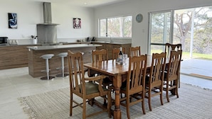 A modern kitchen with a central island, wooden dining table with chairs, and large windows offering a view of the outdoors.