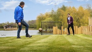 Two people playing soccer on a grassy field with a goalpost, a body of water, and trees in the background. - Superb bespoke lodge with four bedrooms sleeping up to ten people. (Laceby)