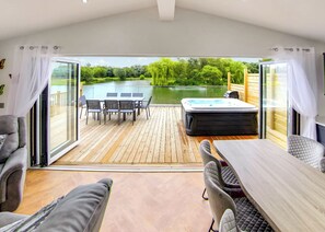 Una terraza con mesa y sillas, un jacuzzi y vistas a un lago y árboles.