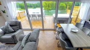 A modern living room with a sofa, a dining table, and chairs, large windows with a view of a pool and deck. - Superb bespoke lodge with four bedrooms sleeping up to ten people. (Laceby)