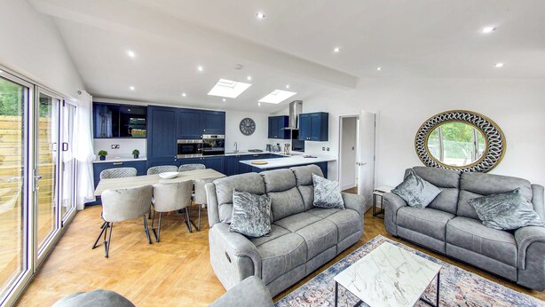 A modern kitchen with dark blue cabinets, a central island, and a dining area with grey sofas and a coffee table. - Superb bespoke lodge with four bedrooms sleeping up to ten people. (Laceby)