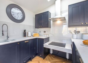 Ett modernt kök med mörka skåp, en vit bänkskiva, en inbyggd spis och en väggklocka.