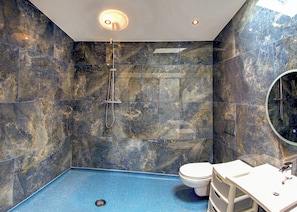 A bathroom with a shower, toilet, and sink, featuring marble walls and a blue floor.