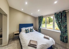 A bedroom with a bed, bedside tables, a window with curtains, and a view of the outdoors.