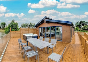A wooden deck with a hot tub, a table, and chairs, and a building with large glass doors.